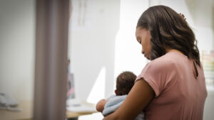 Young mom soothes fussy baby while waiting for doctor stock photo